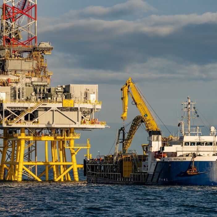 A large blue and white offshore supply vessel, the "Installer," equipped with a yellow crane, positioned alongside a massive yellow offshore platform structure at sea.