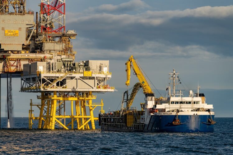 A large blue and white offshore supply vessel, the "Installer," equipped with a yellow crane, positioned alongside a massive yellow offshore platform structure at sea.