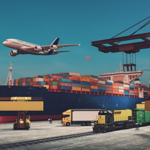 A busy global logistics hub at twilight featuring a large container ship docked at a port, a cargo plane flying overhead, a freight train, a semi-truck, and heavy machinery handling shipping containers under large orange cranes.
