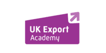 A purple logo consisting of a slanted rectangular banner containing the text "UK Export Academy," with a white arrow pointing diagonally upward in the top right corner.