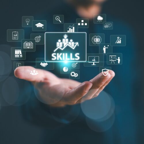 Gemini said A digital composite image of a person's hand held open, with a glowing "SKILLS" icon floating above it. This central icon is surrounded by a cloud of smaller digital symbols representing education, growth, technology, and teamwork, all set against a dark, blurred background with bokeh light effects.