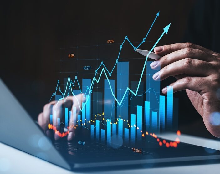 A close-up of hands working on a laptop, with a glowing digital overlay of financial data. The visualization includes rising blue bar charts, upward-pointing line graphs, and numerical data points, illustrating growth and analytics against a dark background.