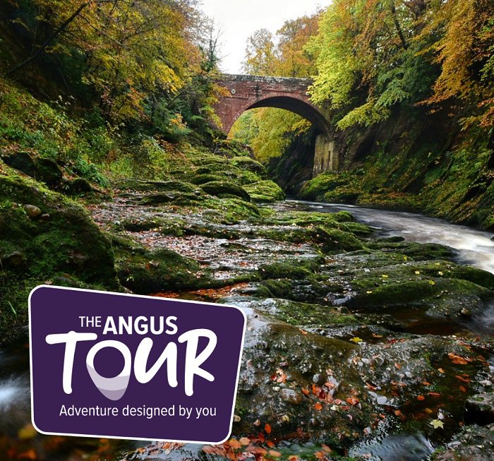 A scenic view of the Rocks of Solitude near Edzell, featured as part of "The Angus Tour." The image shows a river flowing through a deep gorge with moss-covered rocks and vibrant autumn trees. In the background, a high stone arch bridge spans the river. A purple logo in the foreground reads "The Angus Tour: Adventure designed by you."
