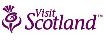 The logo for VisitScotland, featuring the company name in a purple serif font. To the left is a stylized purple thistle icon, with the bulb of the flower shaped into a "v" and "s" monogram.
