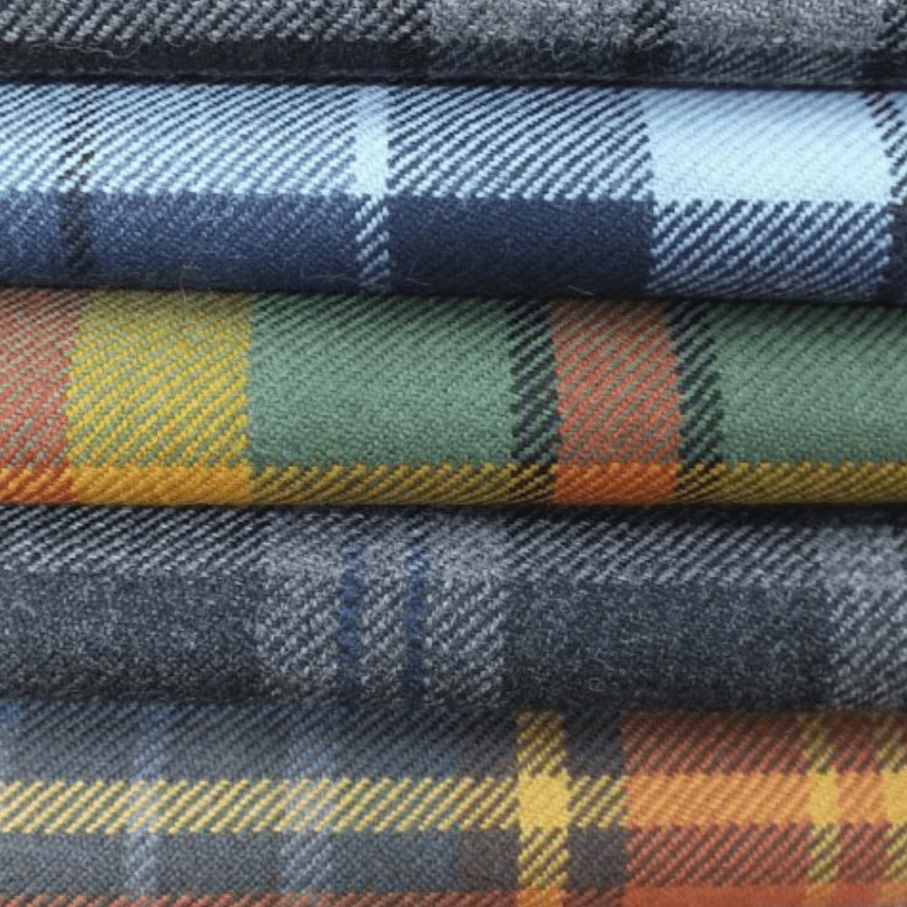 Tartans Collection Cover Image - a stack of folded tartan fabrics featuring various colourways, including blue with light blue stripes, green with yellow and orange stripes, and dark grey with blue accents.