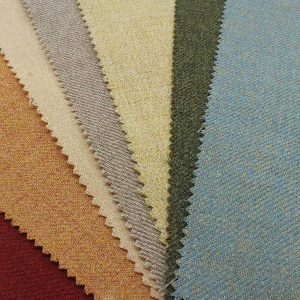Islay Twill Collection Hero photo - a fan of fabric swatches in warm and cool tones, including red, orange, beige, taupe, yellow, green, and blue, each with a subtle textured weave and zig‑zag cut edges.