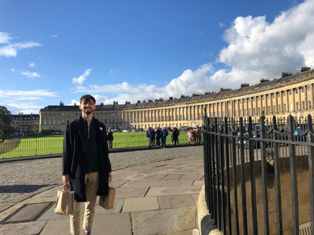 Luc holding brown bags and standing in front of a lawn and row of townhouses.