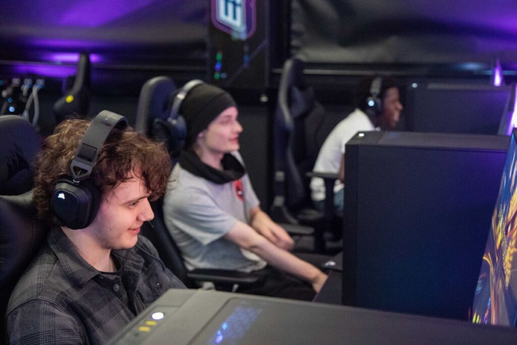 Three students sitting at computers with headphones on in the Esports Hub.