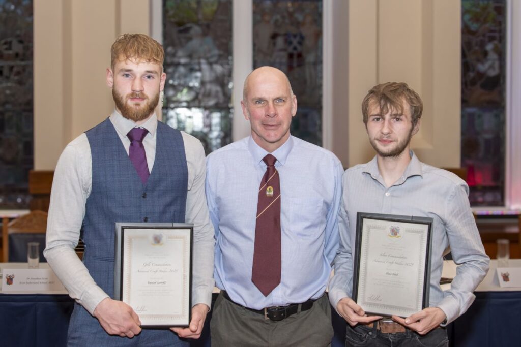 Danny Watson standing in the middle of Daniel Carroll and Chae Reid who are holding certificates.