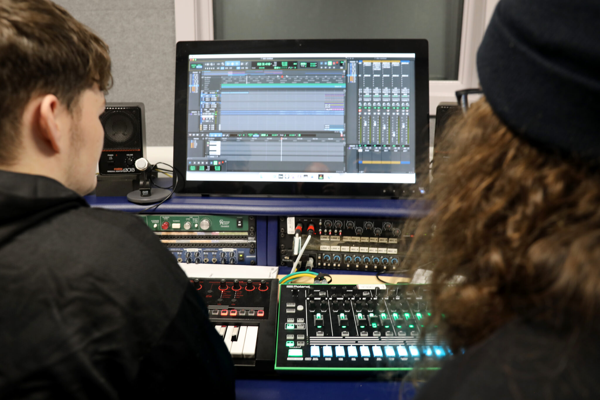 The backs of two students looking at a screen in front of a mixing desk