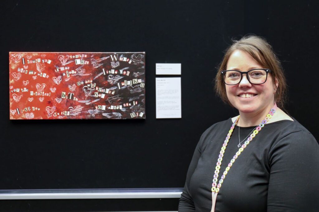 Headshot of Kelly standing in front of her artwork.