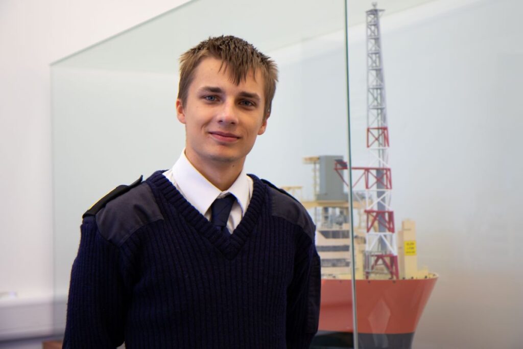 Headshot of Richard in his Deck Officer Cadet uniform in front of a model of a ship.