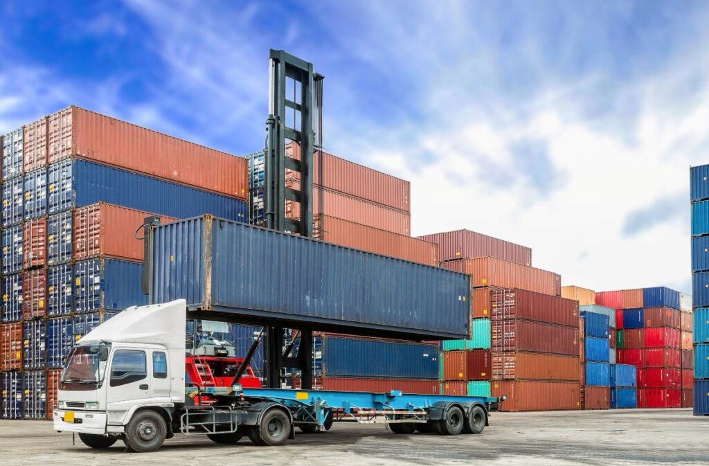 Lorry loading in front of a big stack of cargo containers.