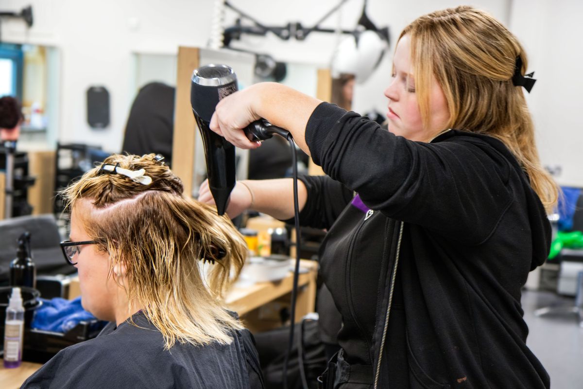 Hairdressing student drying a client's hair in the salon.