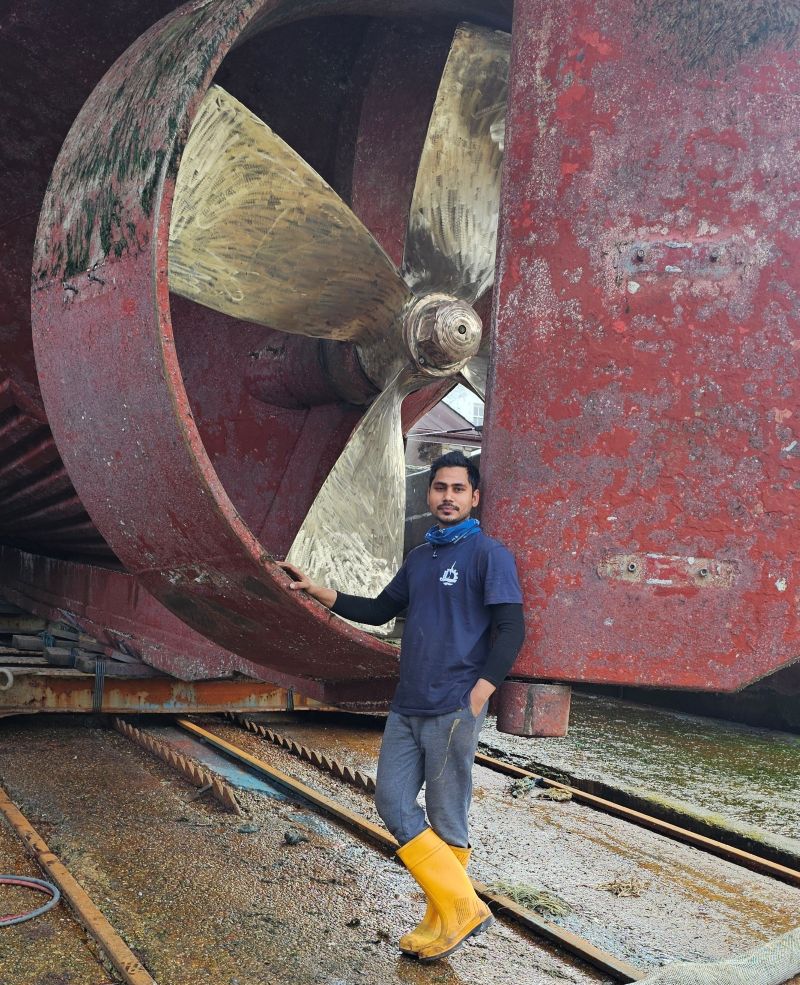 Muhammad standing next to a large ship propeller