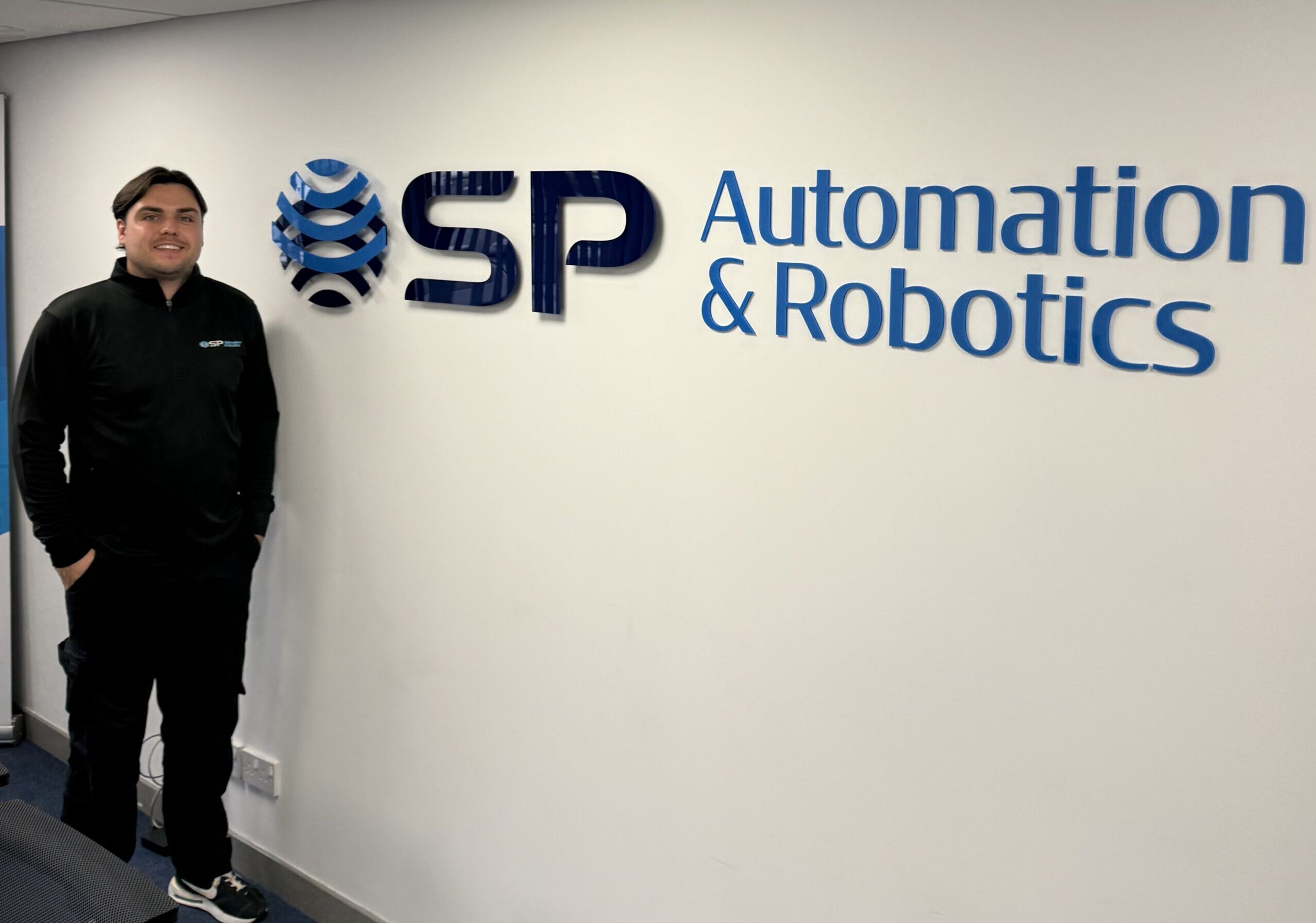 New member of staff leaning against the wall next the the SP Automation & Robotics sign