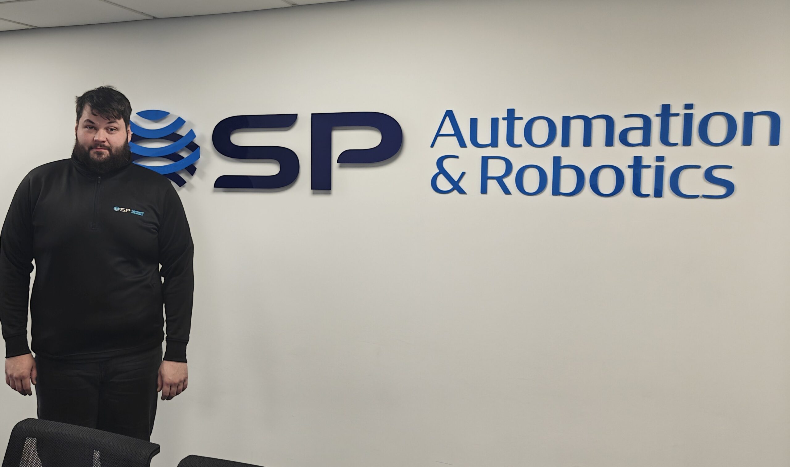 New member of staff leaning against the wall next the the SP Automation & Robotics sign