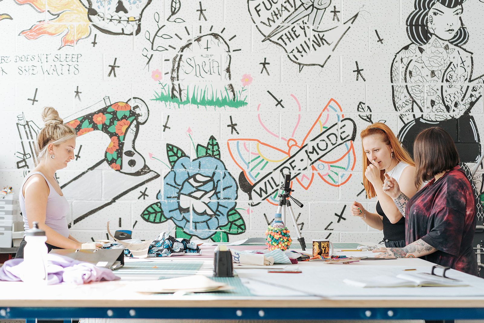 The Circle tenant, Wilde Mode in their unique studio with tattoo like graffiti on the walls. Three people cutting patterns and discussing designs.