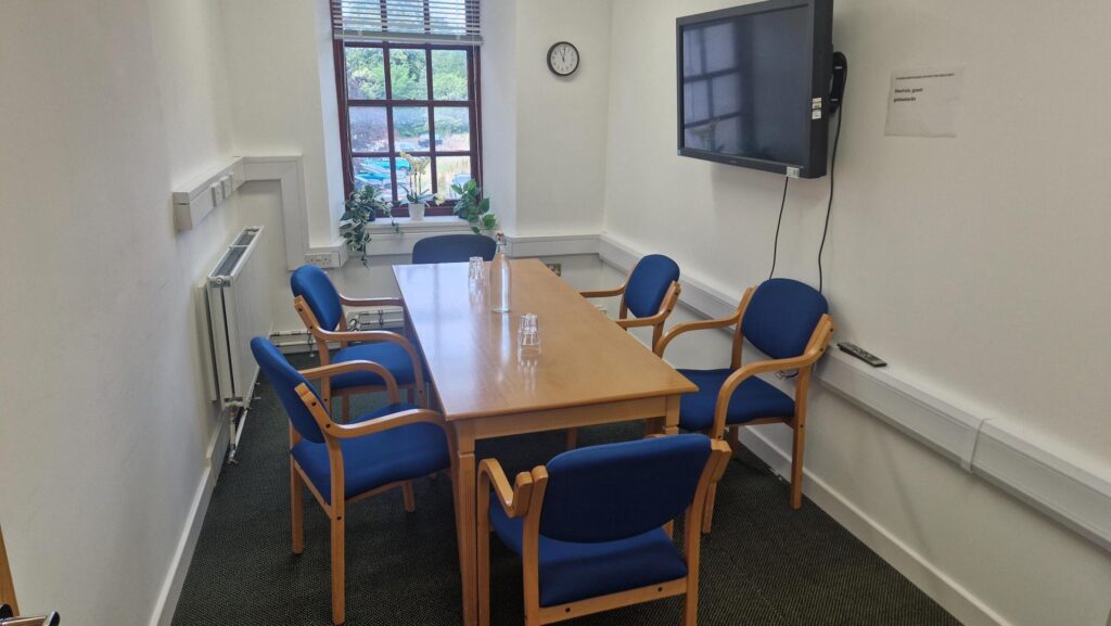 photo of one the meeting spaces in the office. the space fits a table with 6 chairs around it and has a TV mounted on the wall