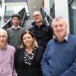 Photo shows 5 people (4 men and 1 women) standing on a staircase