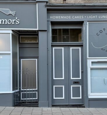The grey storefront of Webmor’s Coffee Shop, featuring white signage for homemade cakes, light lunches, and afternoon teas above a central wooden door and frosted windows.