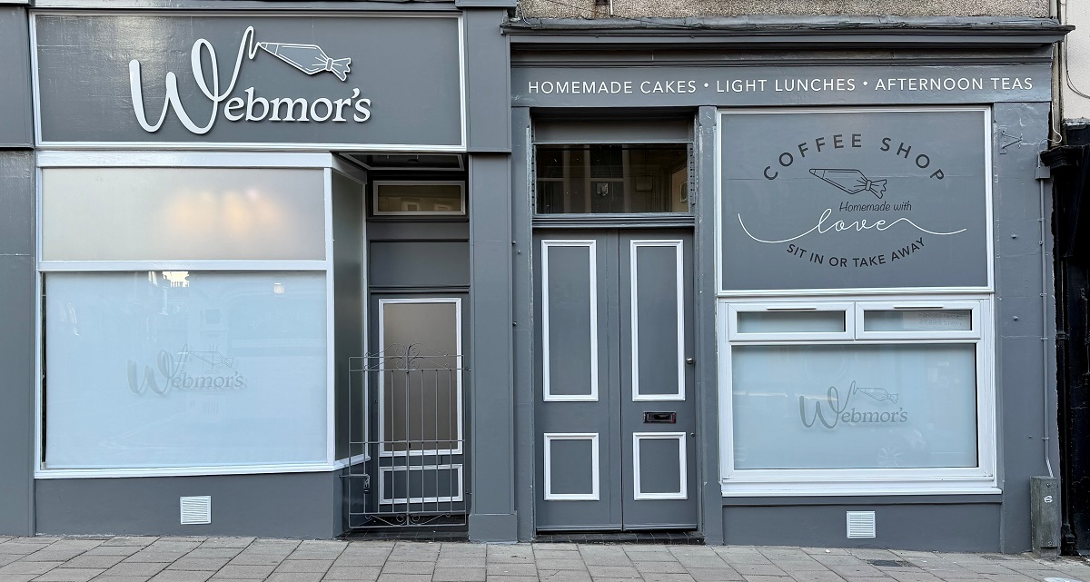 The grey storefront of Webmor’s Coffee Shop, featuring white signage for homemade cakes, light lunches, and afternoon teas above a central wooden door and frosted windows.