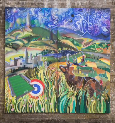 Colourful mural mounted on a brick wall, depicting a stylised Angus landscape with rolling hills, winding paths, trees, a castle, a football pitch and archery target in the foreground, alongside deer hidden among tall grasses beneath a vibrant blue sky filled with abstract patterns and stars.