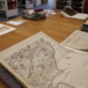 A display table featuring historic documents and an open antique map, with bookshelves visible in the background.