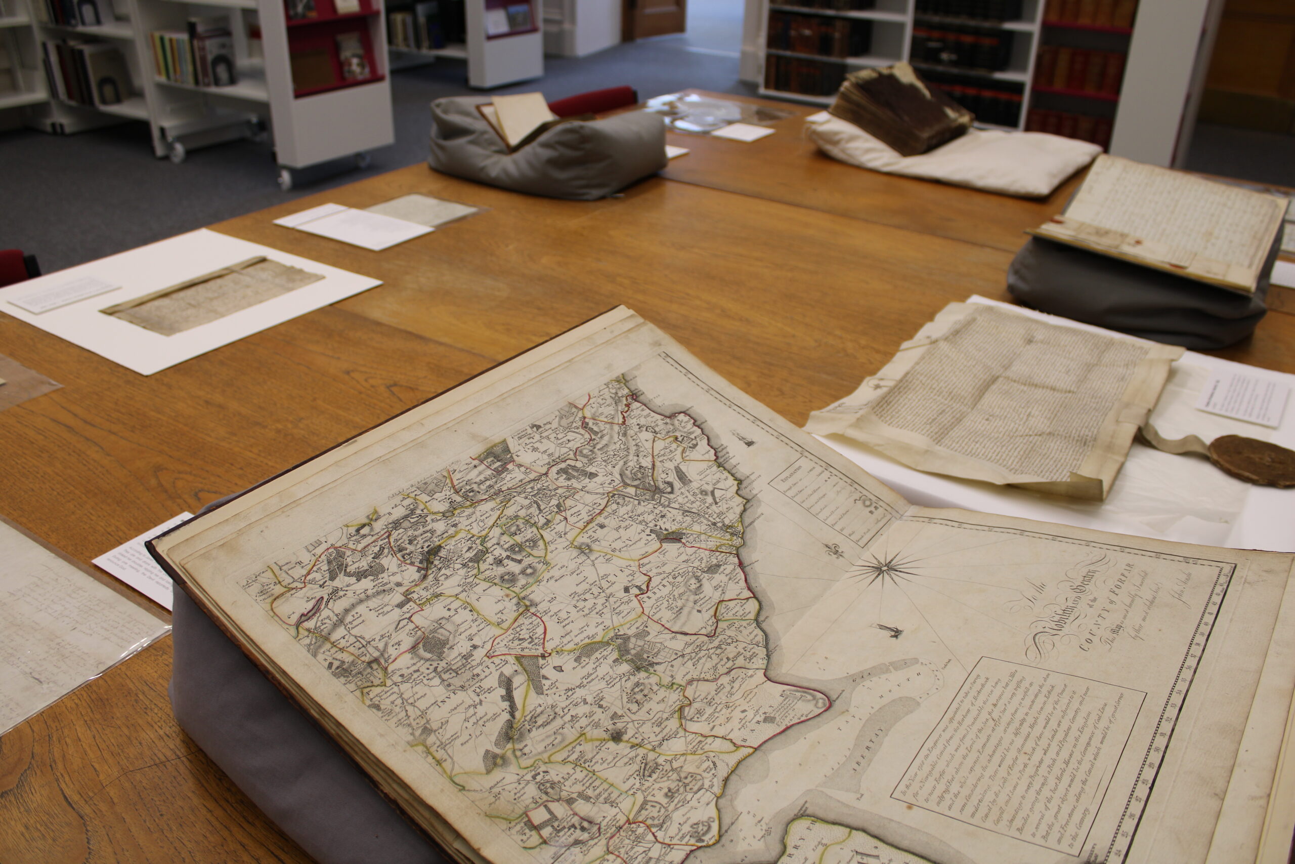 A display table featuring historic documents and an open antique map, with bookshelves visible in the background.