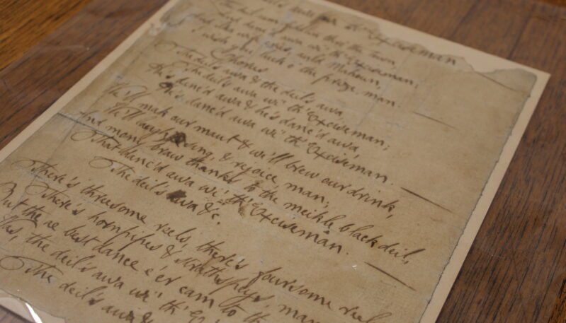 Close-up of a handwritten historical manuscript displayed under a protective cover on a wooden table.
