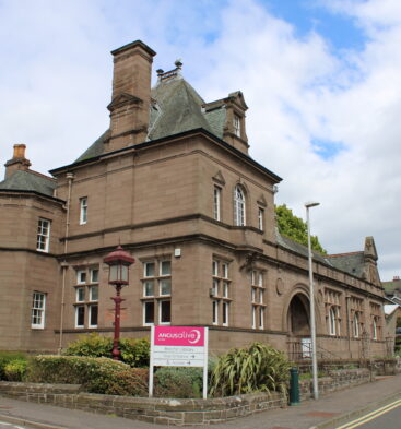 Historic sandstone building housing Brechin Library, featuring decorative architecture, turreted corners and an Angus Alive sign beside a street junction.