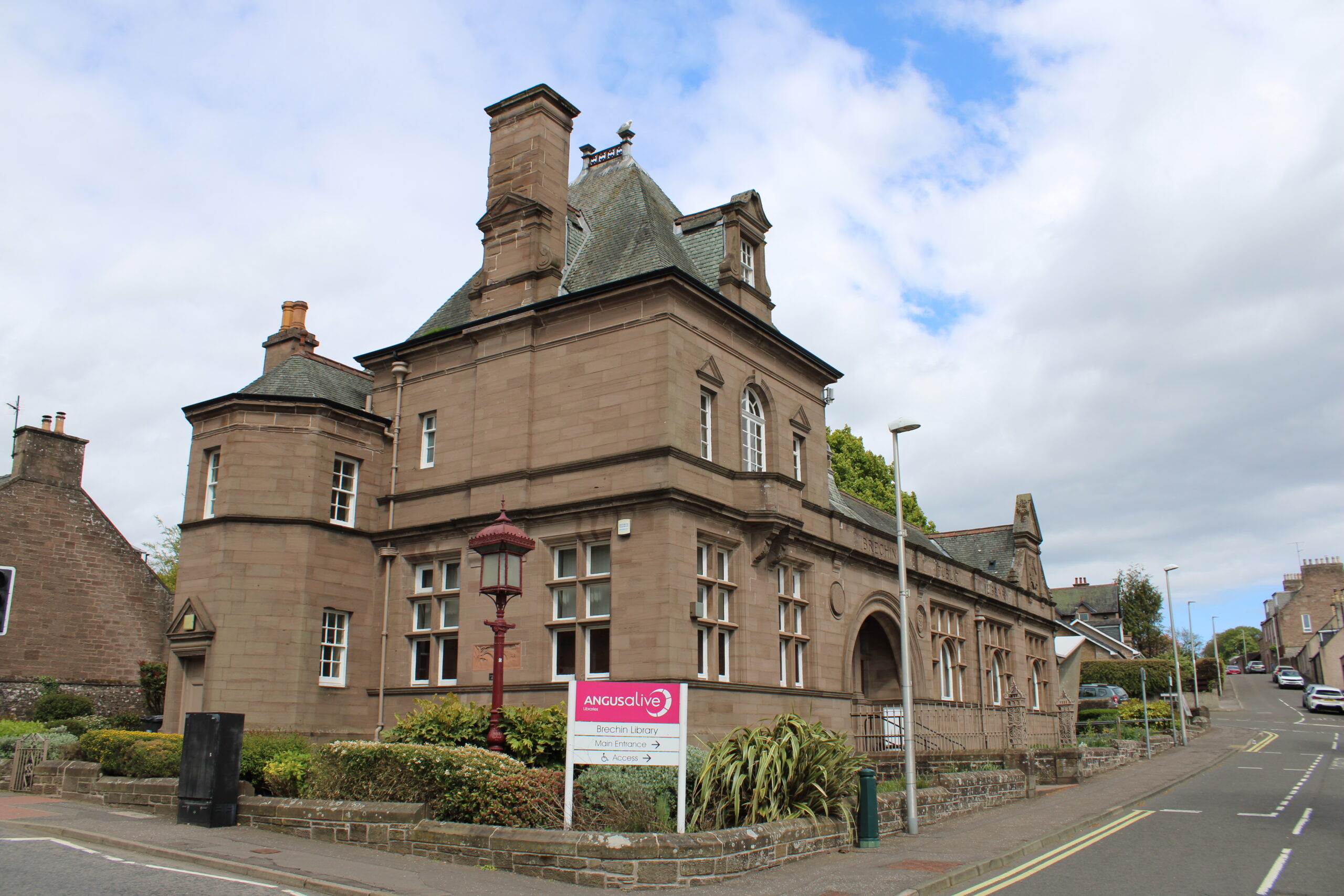 Historic sandstone building housing Brechin Library, featuring decorative architecture, turreted corners and an Angus Alive sign beside a street junction.