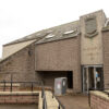 Modern library building in Carnoustie with accessible entrance ramps, stone-clad walls and the words “Carnoustie Library” displayed beneath a civic crest above the entrance.