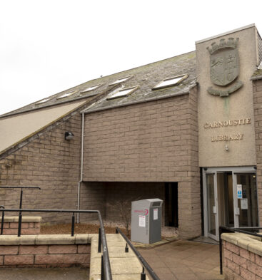 Modern library building in Carnoustie with accessible entrance ramps, stone-clad walls and the words “Carnoustie Library” displayed beneath a civic crest above the entrance.