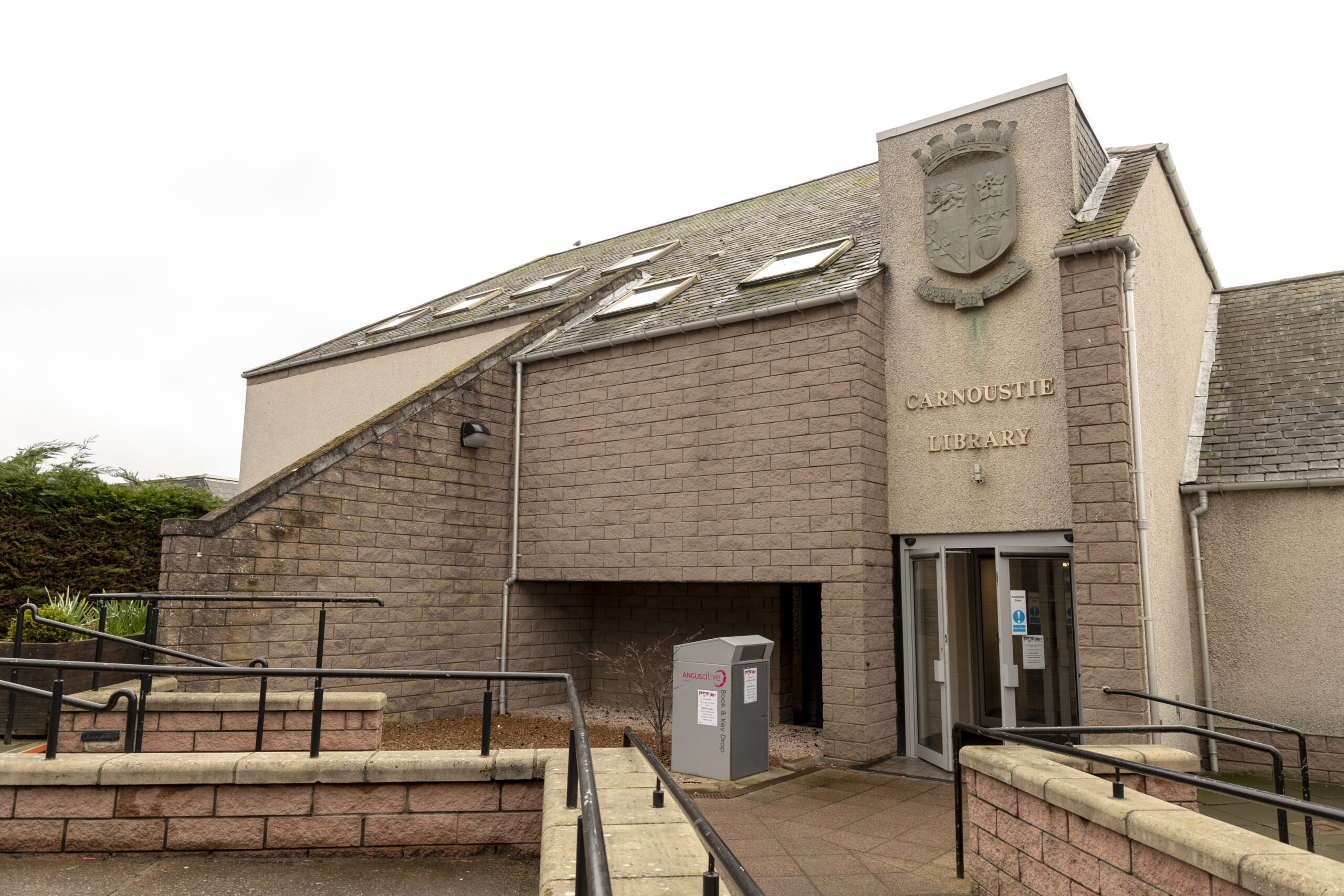Modern library building in Carnoustie with accessible entrance ramps, stone-clad walls and the words “Carnoustie Library” displayed beneath a civic crest above the entrance.