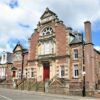 Historic red sandstone library building in Kirriemuir, featuring decorative Victorian architecture, arched windows, stone steps and a prominent central entrance facing the street.