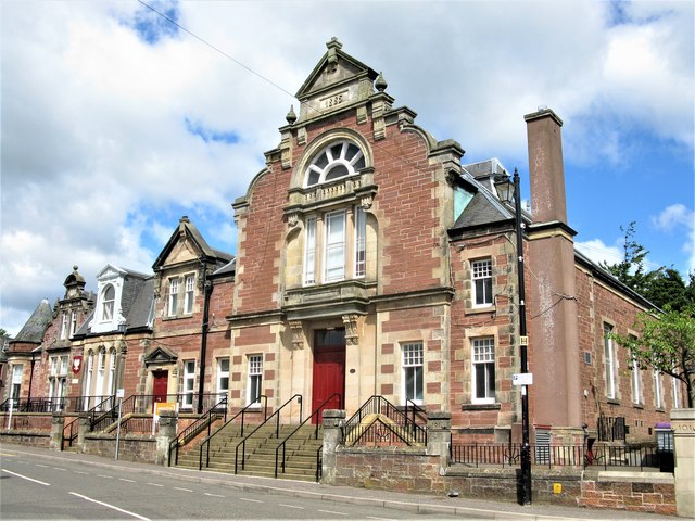 Historic red sandstone library building in Kirriemuir, featuring decorative Victorian architecture, arched windows, stone steps and a prominent central entrance facing the street.