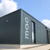 Modern Monifieth Library building with dark metal-clad exterior, large windows and accessible entrance pathways, set beneath a bright blue sky with scattered clouds.