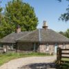 Exterior view of a charming stone cottage with a dark roof and a gravel driveway in bright sunlight.