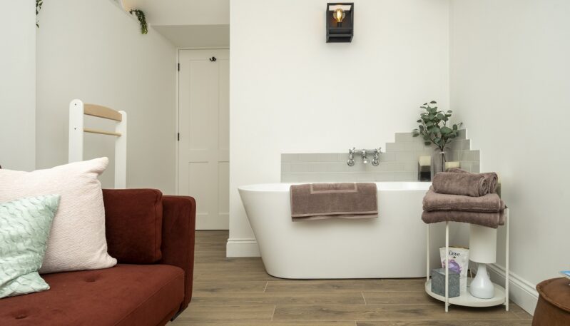 Modern bathroom featuring a freestanding white bathtub, stacked towels, and a partial view of a terracotta sofa.