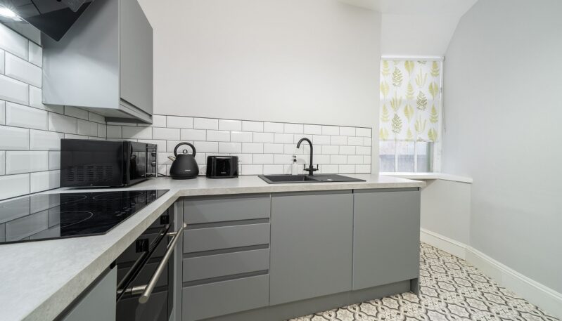 A contemporary kitchen with gray flat-panel cabinets, white subway tile backsplash, patterned floor tiles, and black appliances.