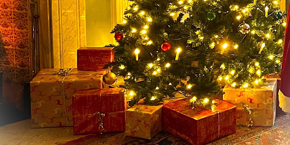 A festive indoor scene showing the base of a Christmas tree adorned with twinkling lights and a few ornaments, with a pile of large red and gold wrapped presents gathered underneath.