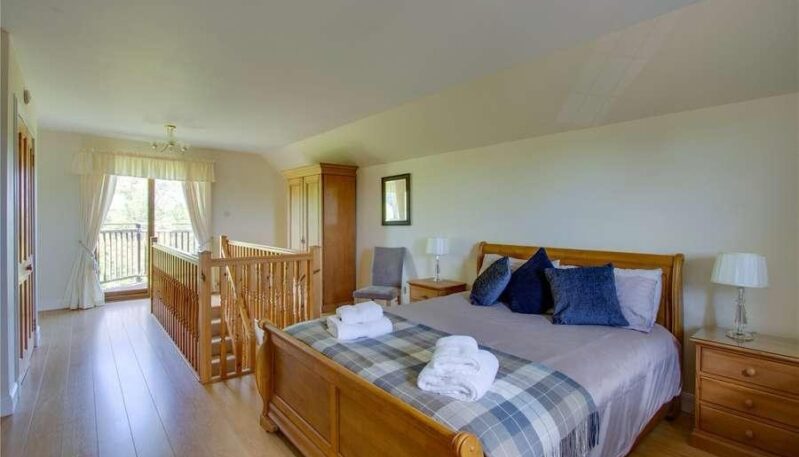 Bright bedroom with light wood flooring, a wooden sleigh bed, a large wooden wardrobe, and an open landing/balcony area with wooden railings.