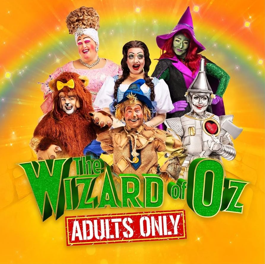 A poster for a pantomime show titled "The Wizard of Oz: Adults Only." Six performers in colorful costumes and exaggerated makeup are posing in a group, set against a vibrant yellow-orange background with a rainbow arc above them. The characters include an adult-panto version of the Dame, Dorothy, the Wicked Witch of the West, the Cowardly Lion, the Scarecrow, and the Tin Man.