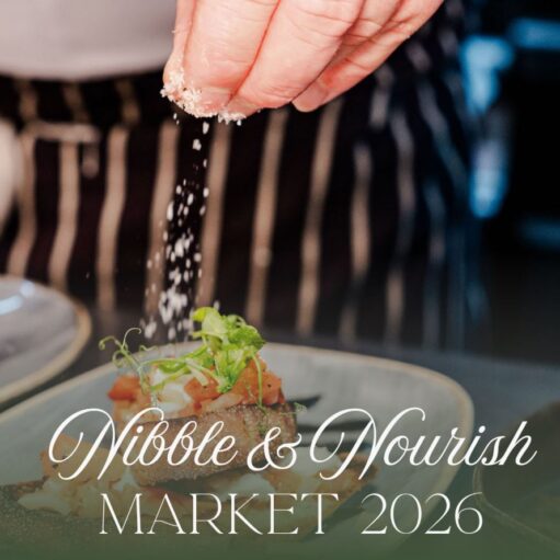 A close-up photograph of a chef's hand sprinkling white shavings, likely cheese, onto a small plated food item topped with garnish. White cursive text overlaid on the image reads "Nibble & Nourish" and "MARKET 2026" below it.