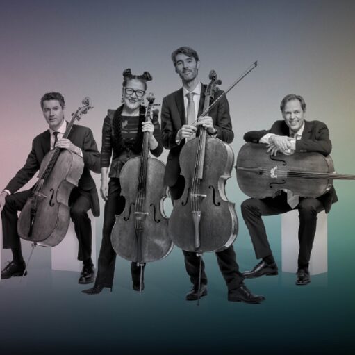 A black-and-white photograph of a four-person cello ensemble posed against a vibrant, multi-colored gradient background. Two musicians are seated and two are standing, all holding their cellos, dressed in formal dark attire.