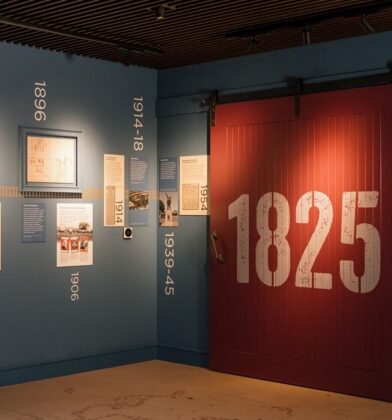 A historical timeline wall in the visitor center painted deep blue, decorated with dates, vintage photos, and a large sliding red barn door with "1825" printed on it in white.