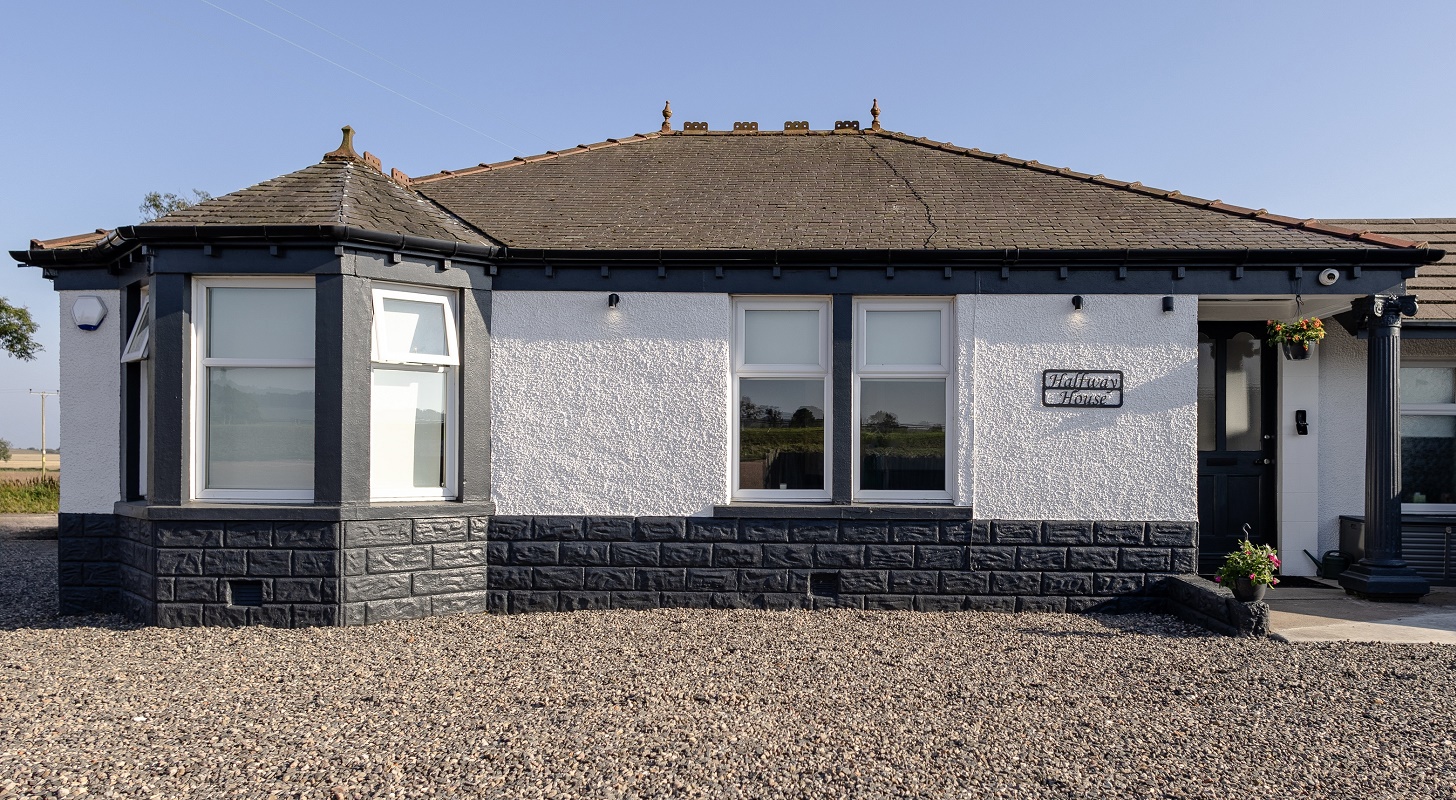 Exterior view of a modern single-story bungalow with white walls, dark gray stone detailing, and a gravel front garden.