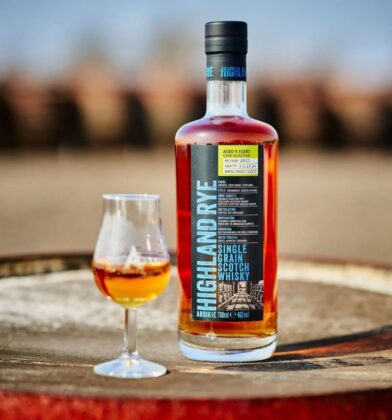 A bottle of Arbikie Highland Rye Single Grain Scotch Whisky stands next to a tasting glass on a wooden barrel.