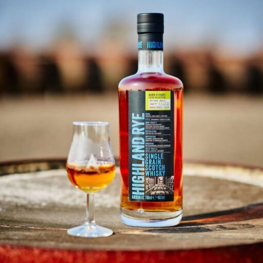 A bottle of Arbikie Highland Rye Single Grain Scotch Whisky stands next to a tasting glass on a wooden barrel.